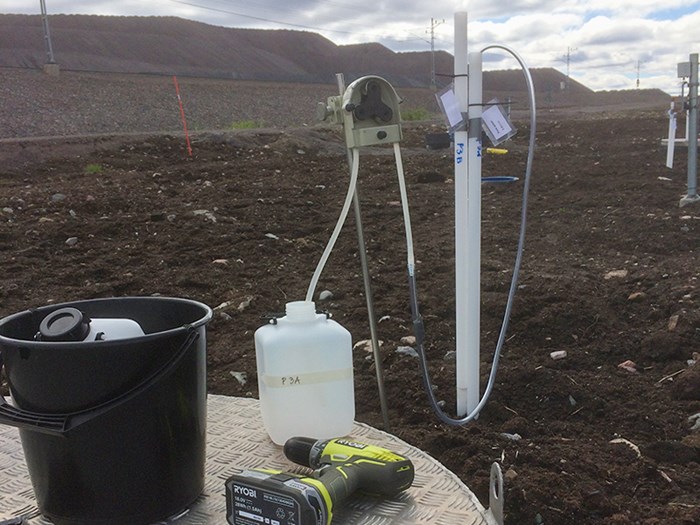 En hink, en borrmaskin och en vattendunk vid vetenskaplig utrustning på jordig mark. Foto.
