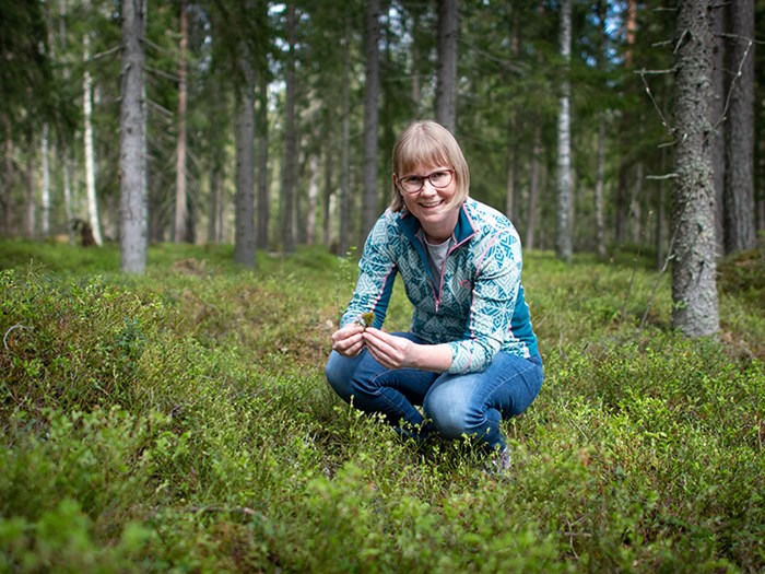 En kvinna sitter på huk i skogen. Foto.