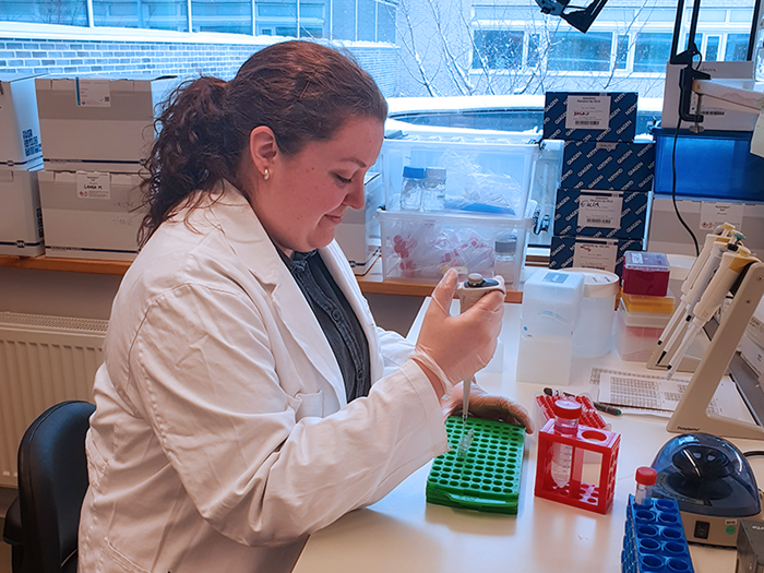 A woman is pipetting by a lab bench. Photo.