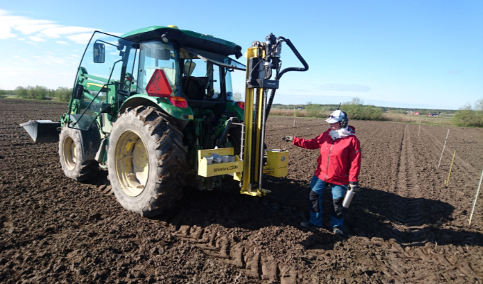 En traktor med ett rör bakom, på ett brunt fält. Foto.