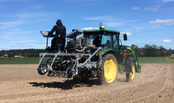 En traktor som drar en såmaskin på vilken det sitter en person. Foto.