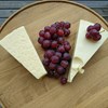 Two pieces of hard cheese and a cluster of grapes on a wooden tray. Photo.