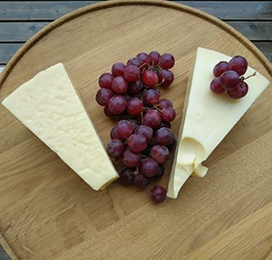 Two pieces of hard cheese and a cluster of grapes on a wooden tray. Photo.
