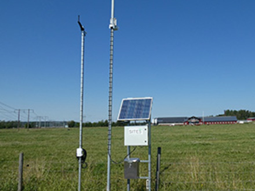 A mast with a camera by a field. Photo.