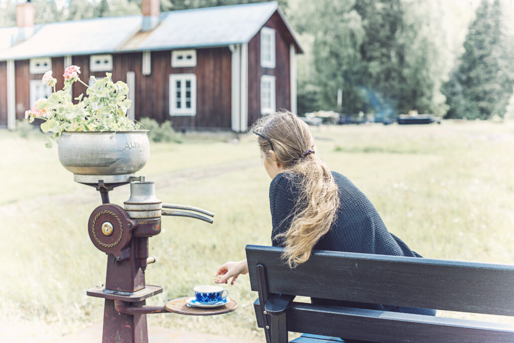 Kvinna sittande framför gammal Västerbottensgård