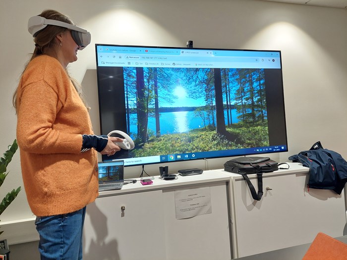 Kvinna som bär VR-glasögon bredvid en skärm med naturmotiv