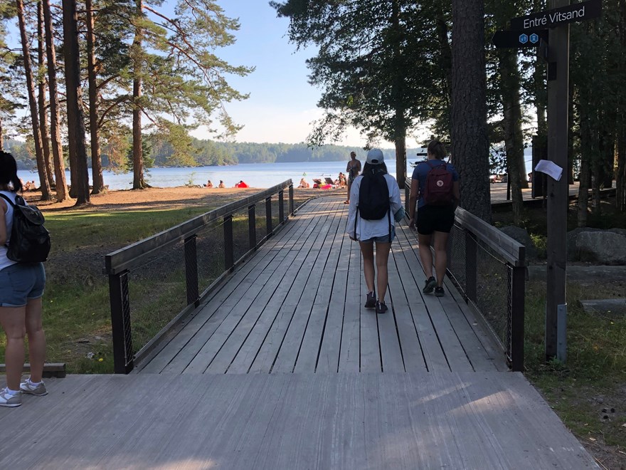 People walking on a wooden trail towards a  lake