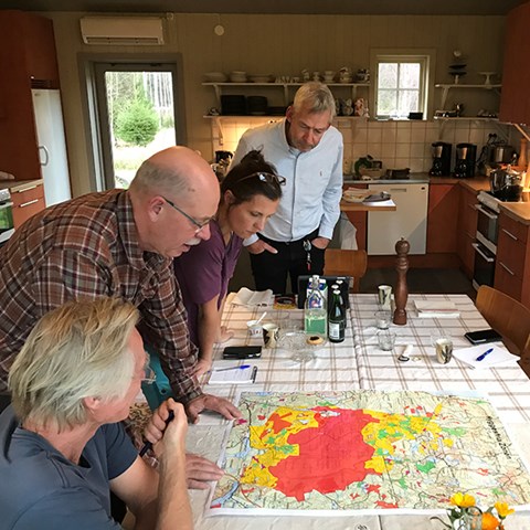 Fyra personer står böjda över ett köksbord och tittar på en karta. Foto.