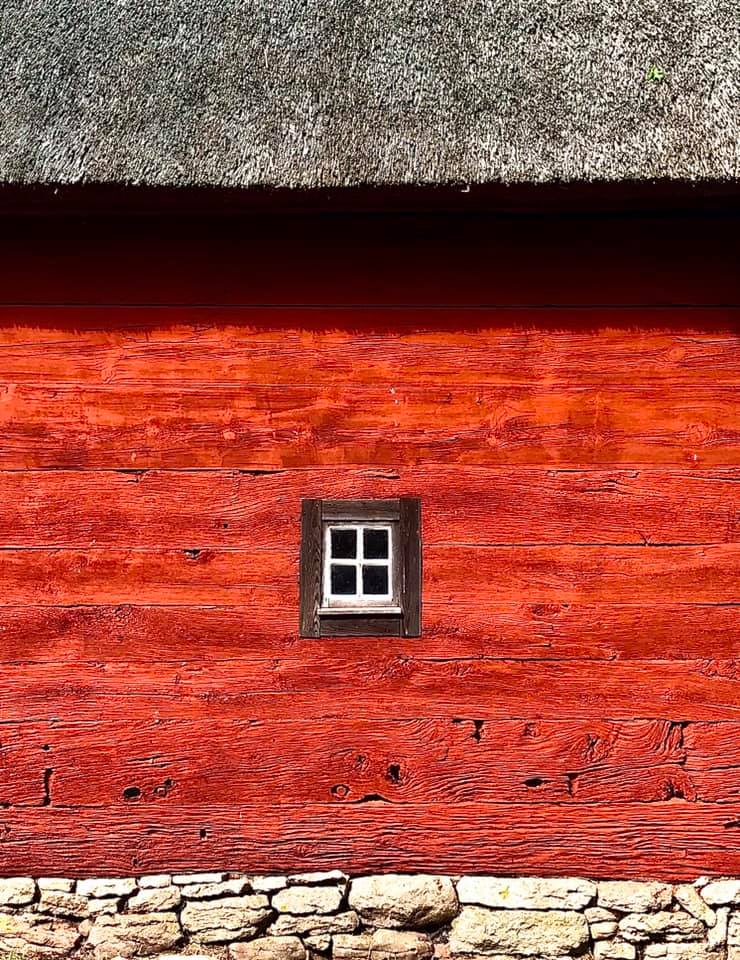 Ett äldre rött hus, med stengrund, grästak och ett litet fönster