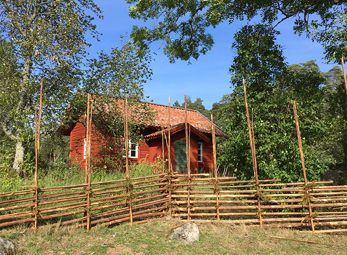 A croft on small hill behind a roundpole fence. Photo.