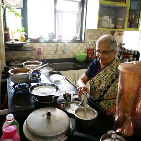 En äldre kvinna i Indien lagar mat vid spisen i köket