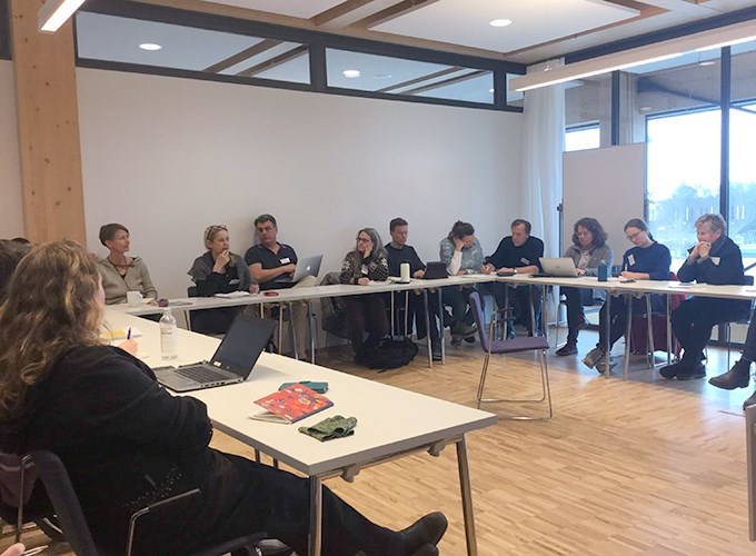 En undervisningssal med bord i u-sittning och människor som samtalar. Foto.