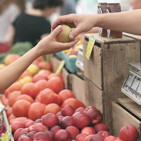 En kvinna köper ett äpple vid ett marknadsstånd. Foto.