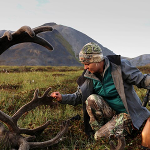 A female hunter kneeling beside a shot caribou. Photo.