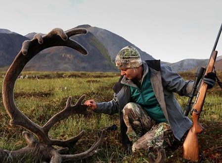 A female hunter kneeling beside a shot caribou. Photo.
