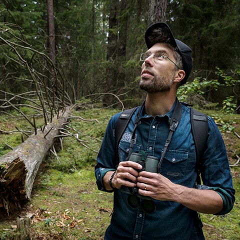 Foto på Marcus Hedblom i skogen med en kikare i händerna