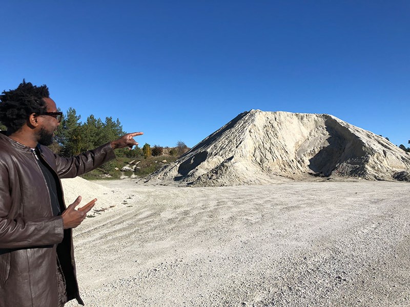 En man pekar på en sandhög i ett sandtag. Foto.