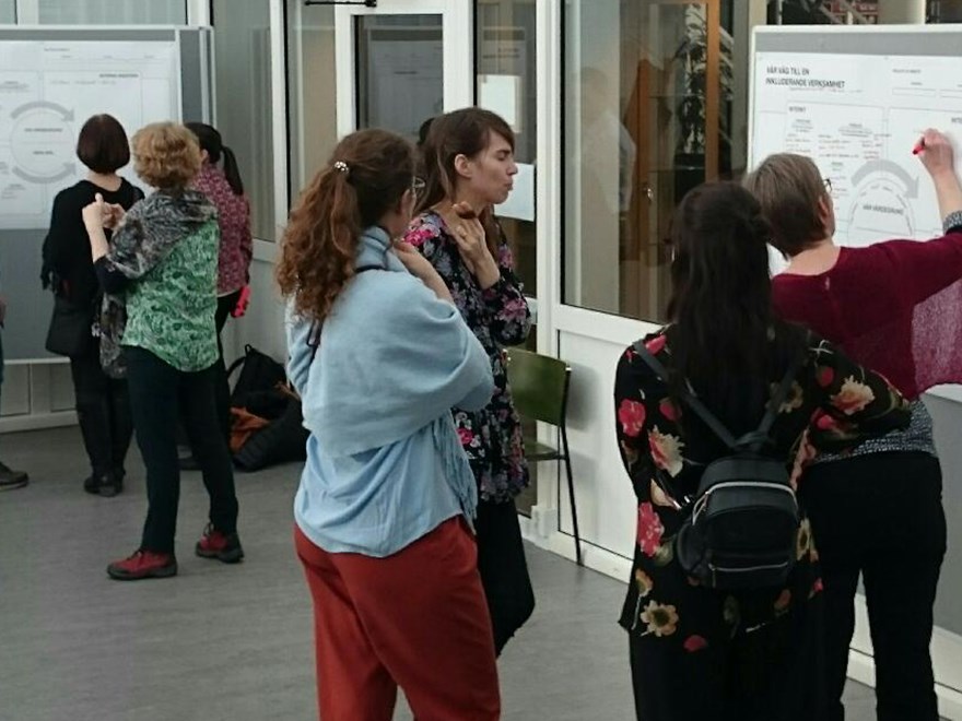 Personer står framför en whiteboard tavla och diskuterar, foto.
