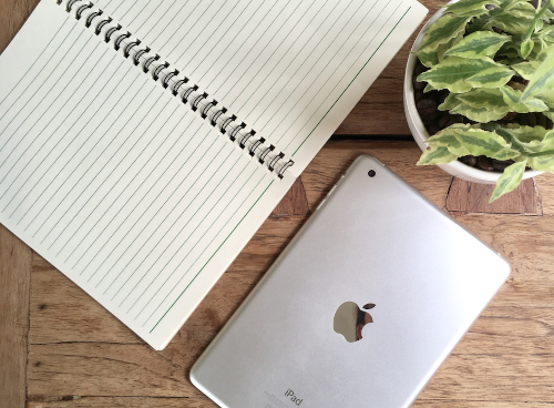 Ett bord med ett anteckningsbok, en iPad och en krukväxt