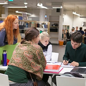 Fyra personer tittar i en bok tillsammans. Foto.