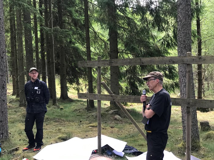 Två personer framför publik i skog. Foto.