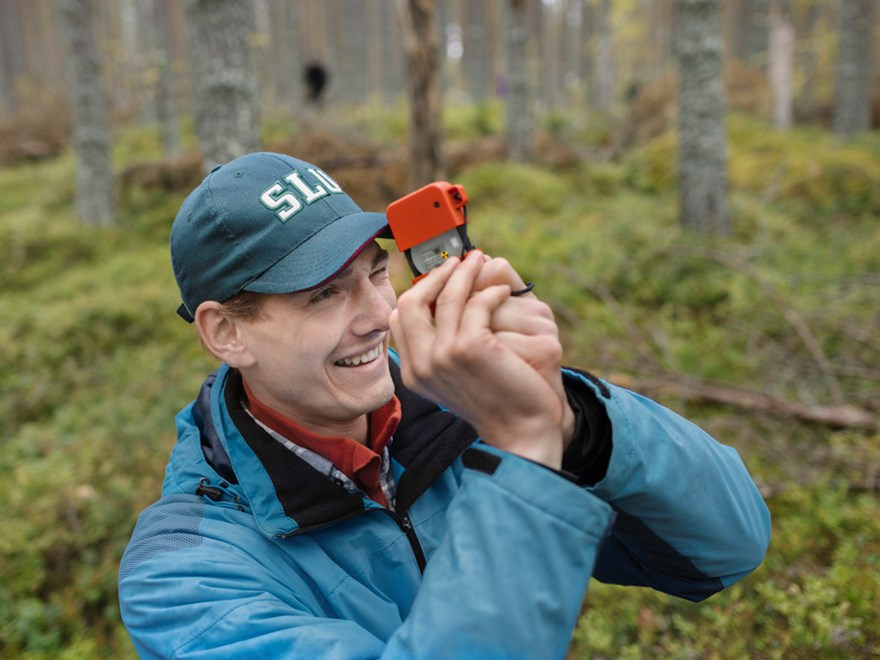 En man tittar genom en slags kikare i skog. Foto.