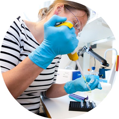 En kvinna pipetterar i ett lab. Foto.