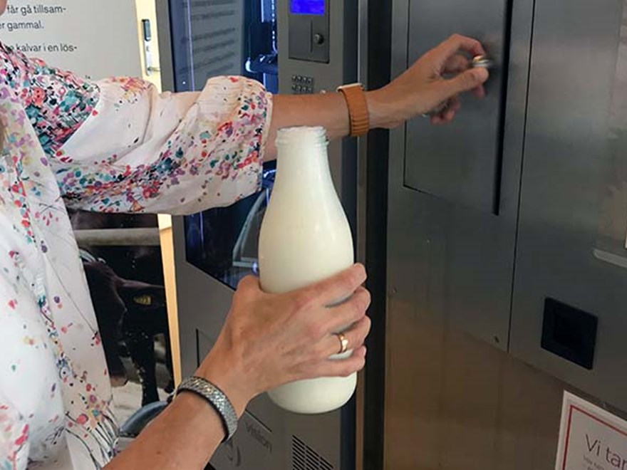 Närbild på en hand som  håller i en flaska mjölk vid mjölkautomaten. Foto.