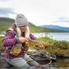 Kvinna vid vatten håller i en fisk. Foto.