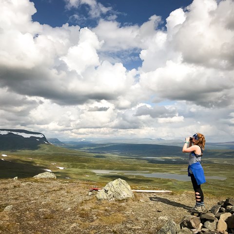 Kvinna med kikare i fjällandskap. Foto.