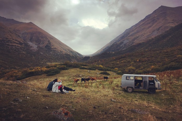 Fikapaus i med berg i bakgrunden, boskap som betar och en bild som står parkerad.