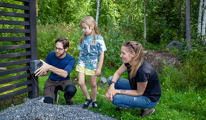 Two adults and a child putting up a wildlife camera in a garden. Photo.