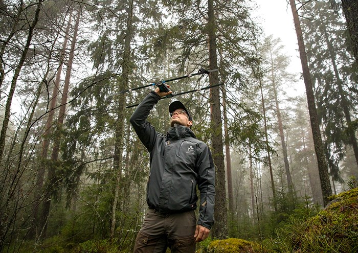 Fredrik i skog, håller upp pejlingsutrustning ovanför huvudet. Foto.