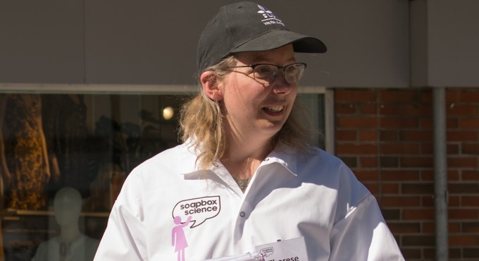 Therese iförd vitt labbrock håller en presentation utomhus. Foto.
