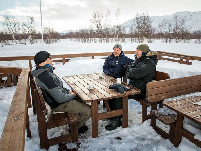 Personer samtalar vid ett bord utomhus i vinterlandskap. Foto.