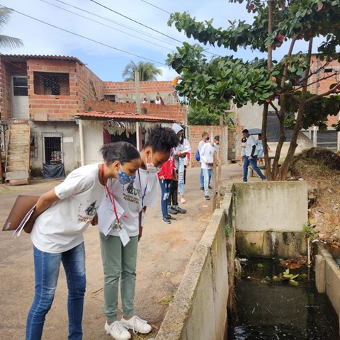  Young people with face masks look at an open drain.