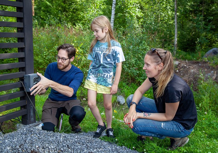 Three people set up a wildlife camera in a garden.