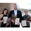 Tre pristagare med blommor och diplom.
