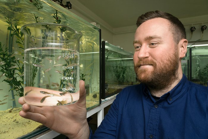 Michael håller upp ett mätglas med små fiskar i.
