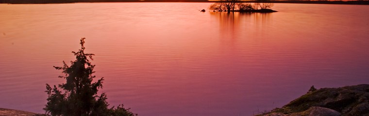 Solnedgång över sjö. Foto.