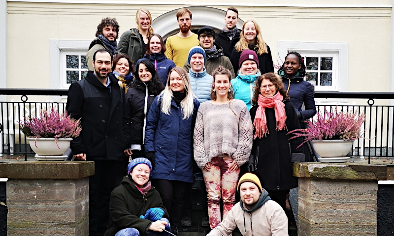 16 standing and 2 sitting persons on a stair outside a manor house. Group photo.