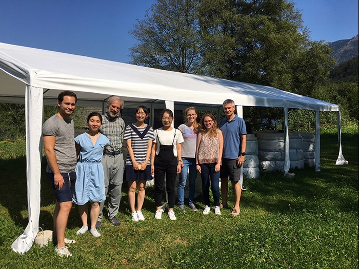 Eight persons standing in front of a tent roof shading mesocosms. Group photo.