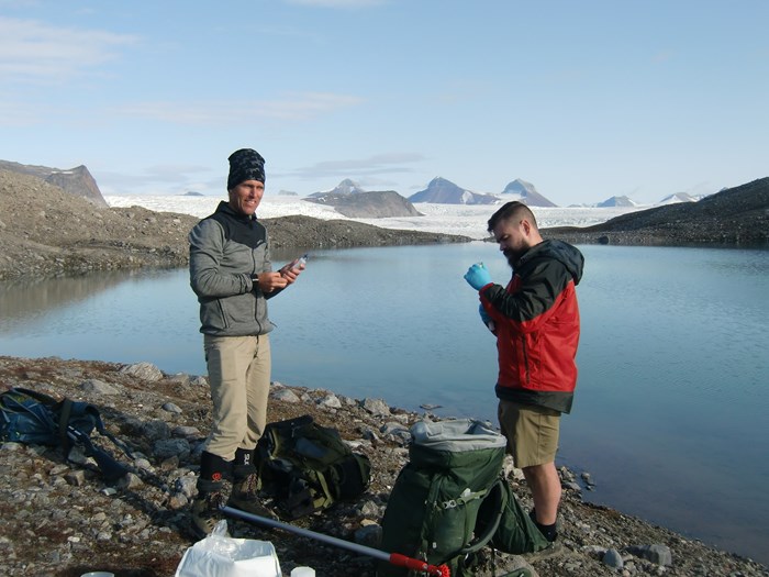 Two people preparing sampling by a lake. Photo.