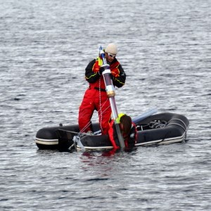 Two persons in a rubber boat. One of them is standing and is holding a long sediment tube. Photo.