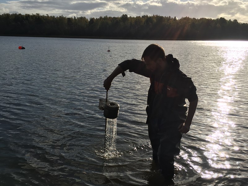 En man tar ett vattenprov i en sjö. Foto.