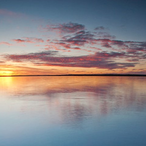 Solnedgång över sjö. Foto.