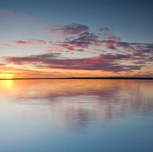Solnedgång över sjö. Foto.
