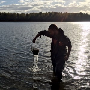 Person, in backlight, taking samples standing in the water. Photo.
