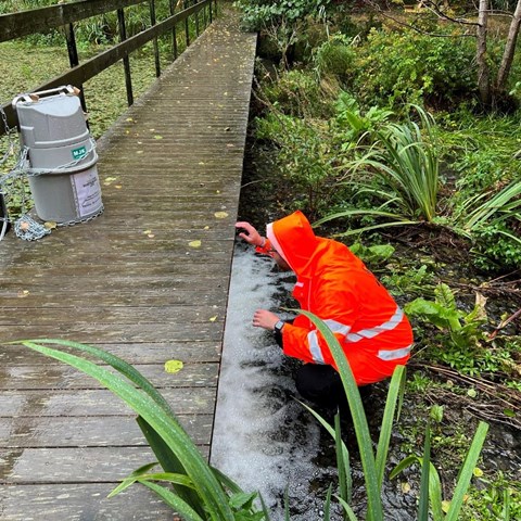 Man in raincoat kneels by bridge. Photo.