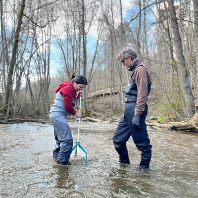 Two persons standing in stream to sample. Photo.